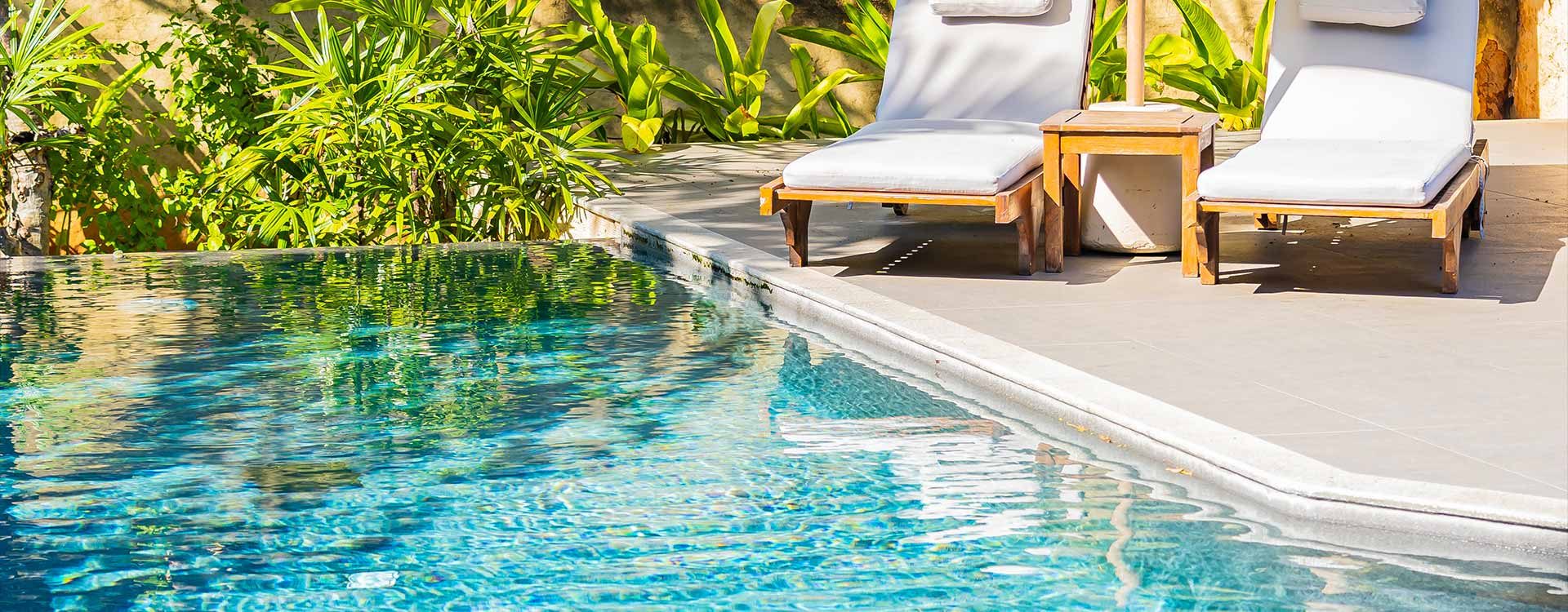 Piscine extérieure bordée de transats au milieu d'un jardin tropical