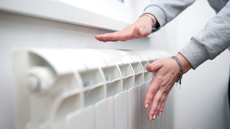 Mains posées sur un radiateur chaud alimenté par une pompe à chaleur